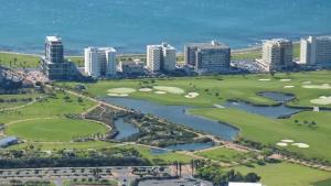 Vue aérienne d'un terrain de golf en bord de mer avec plusieurs immeubles modernes alignés face à l'océan