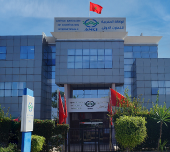 Façade du siège de l’Agence Marocaine de Coopération Internationale (AMCI) à Rabat, surmontée du drapeau du Maroc et entourée de jardins entretenus.