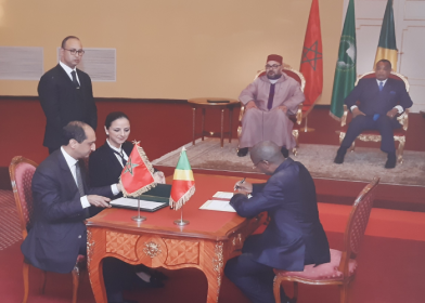 Signature d’un accord entre des représentants du Maroc et du Congo, en présence du roi Mohammed VI et du président congolais Denis Sassou-Nguesso, assis derrière eux, avec les drapeaux nationaux en arrière-plan.
